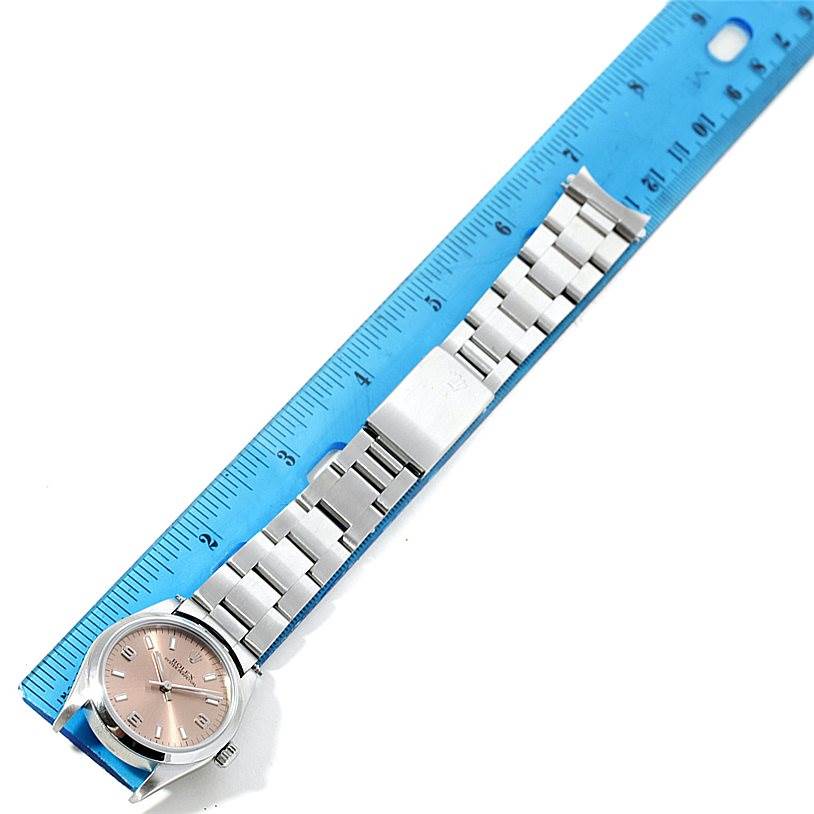 The image shows a Rolex Mid-Size 77080 Women's Stainless Steel Pink Dial 77080 Women's Stainless Steel Pink Dial watch laid flat next to a ruler, displaying the face and metal strap.