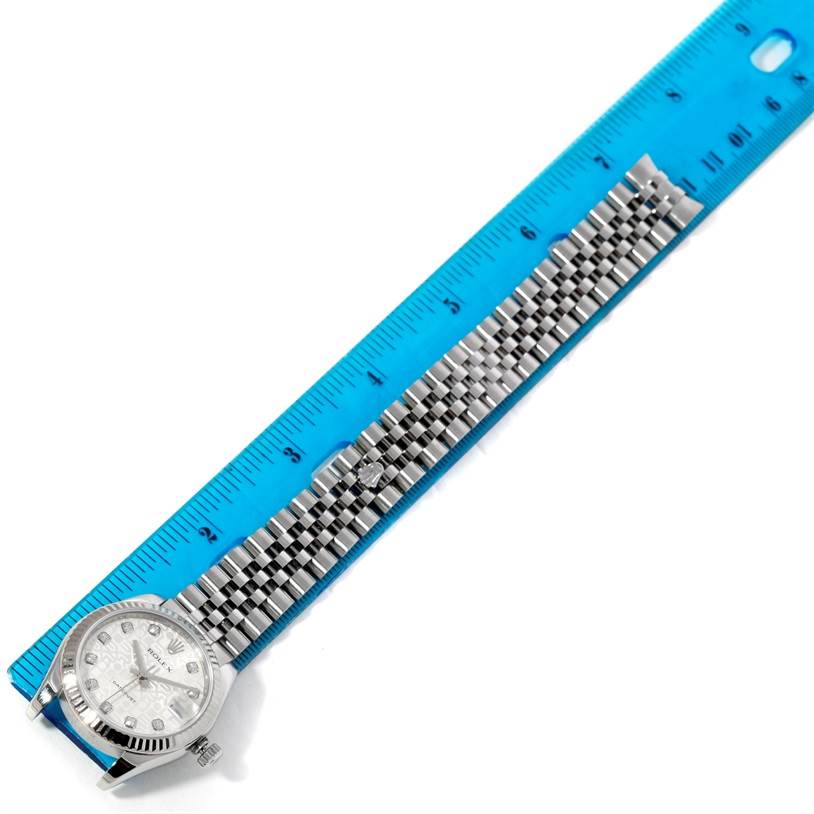 The image shows a Mid-Size Rolex watch with its face and bracelet laid flat next to a blue ruler, displaying its length.