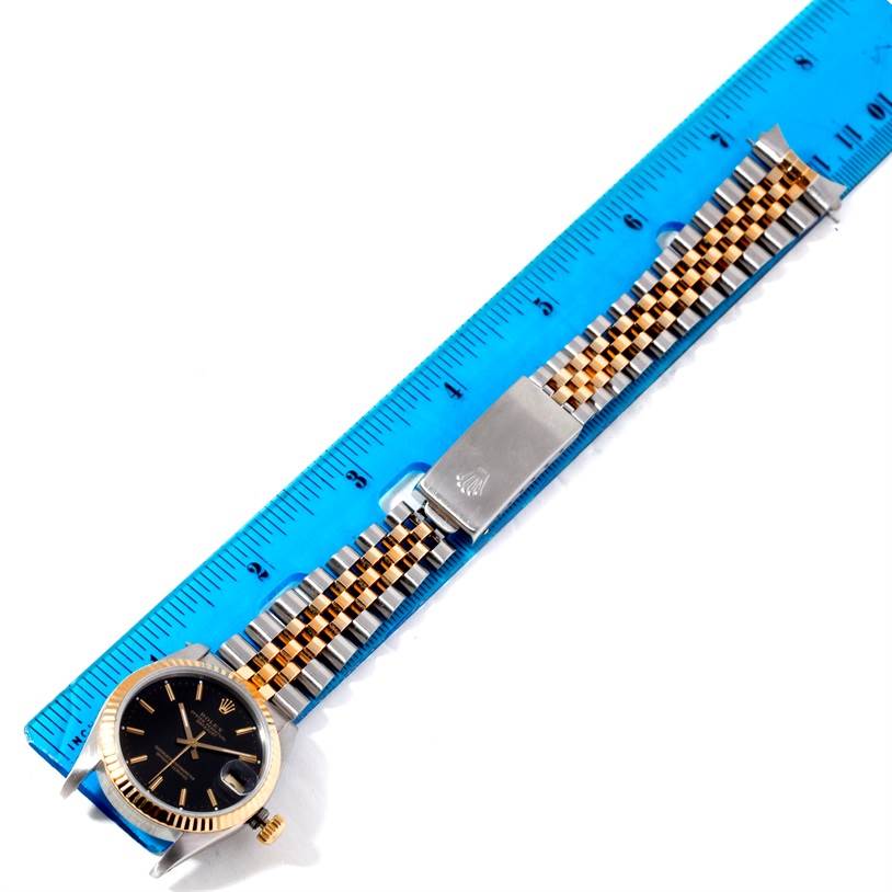 This image shows a side angle of a Mid-Size Rolex watch, highlighting the face, bezel, and metal bracelet with a ruler for scale.