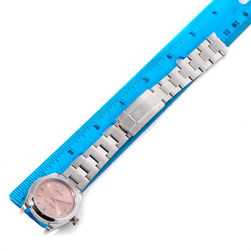 The image shows a top-down view of a Rolex Mid-Size 177200 Women's Stainless Steel Pink Dial 177200 Women's Stainless Steel Pink Dial model watch with a silver band and pink dial, placed next to a ruler.