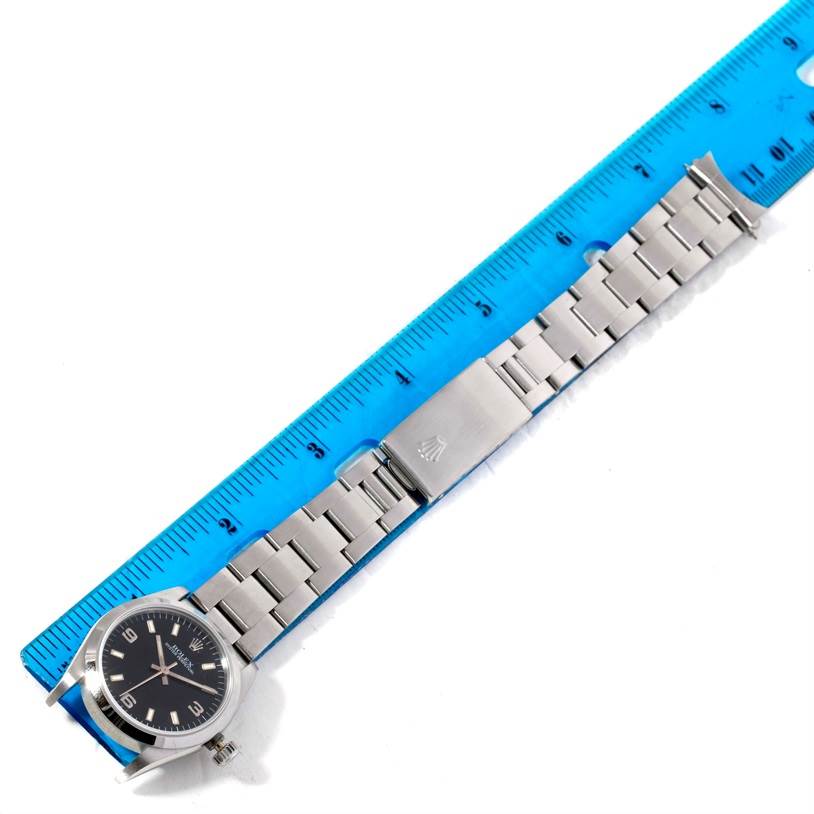 The Rolex Mid-Size 67480 Women's Stainless Steel Black Dial 67480 Women's Stainless Steel Black Dial watch is shown flat, displaying its face, bracelet, and clasp next to a blue ruler for size reference.