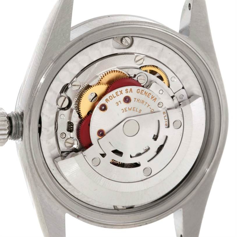 The image shows the inner mechanical movement of a Mid-Size Rolex watch, captured from the back with parts such as gears and jewels visible.
