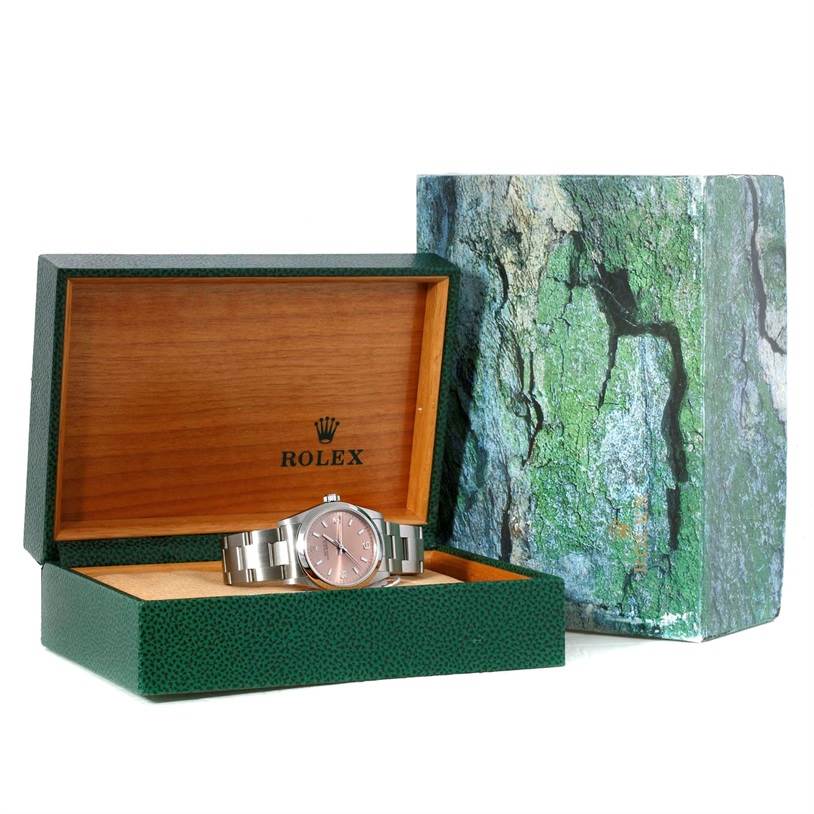 The image shows a Rolex Mid-Size 77080 Women's Stainless Steel Pink Dial 77080 Women's Stainless Steel Pink Dial watch in an open green and wooden box, with its outer packaging beside it.
