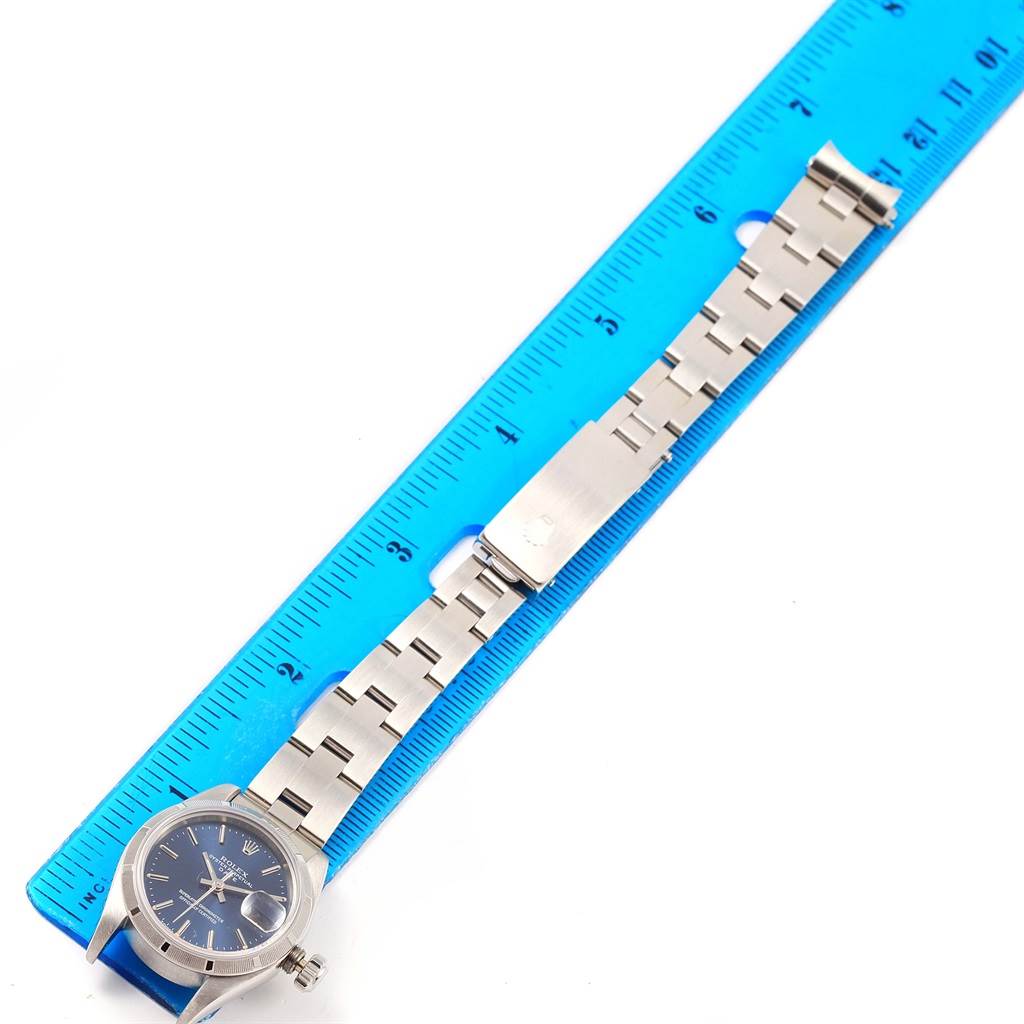 The image shows a Rolex Date 69190 Women's Stainless Steel Blue Dial 69190 Women's Stainless Steel Blue Dial model watch laid flat with the metal bracelet extended next to a blue ruler.