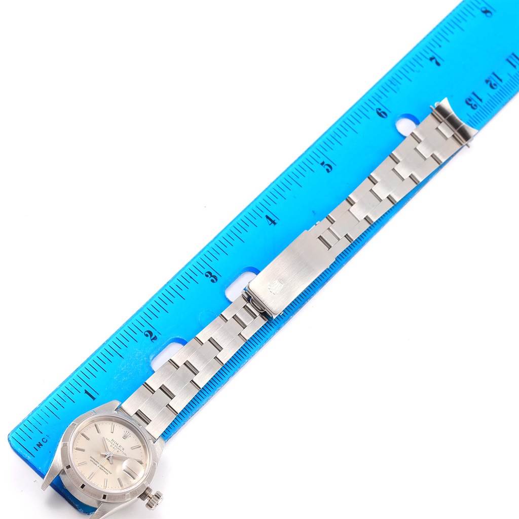 The image shows the front view of a Rolex Date 69190 Women's Stainless Steel Silver Dial 69190 Women's Stainless Steel Silver Dial watch placed next to a blue ruler, displaying the watch face and band.
