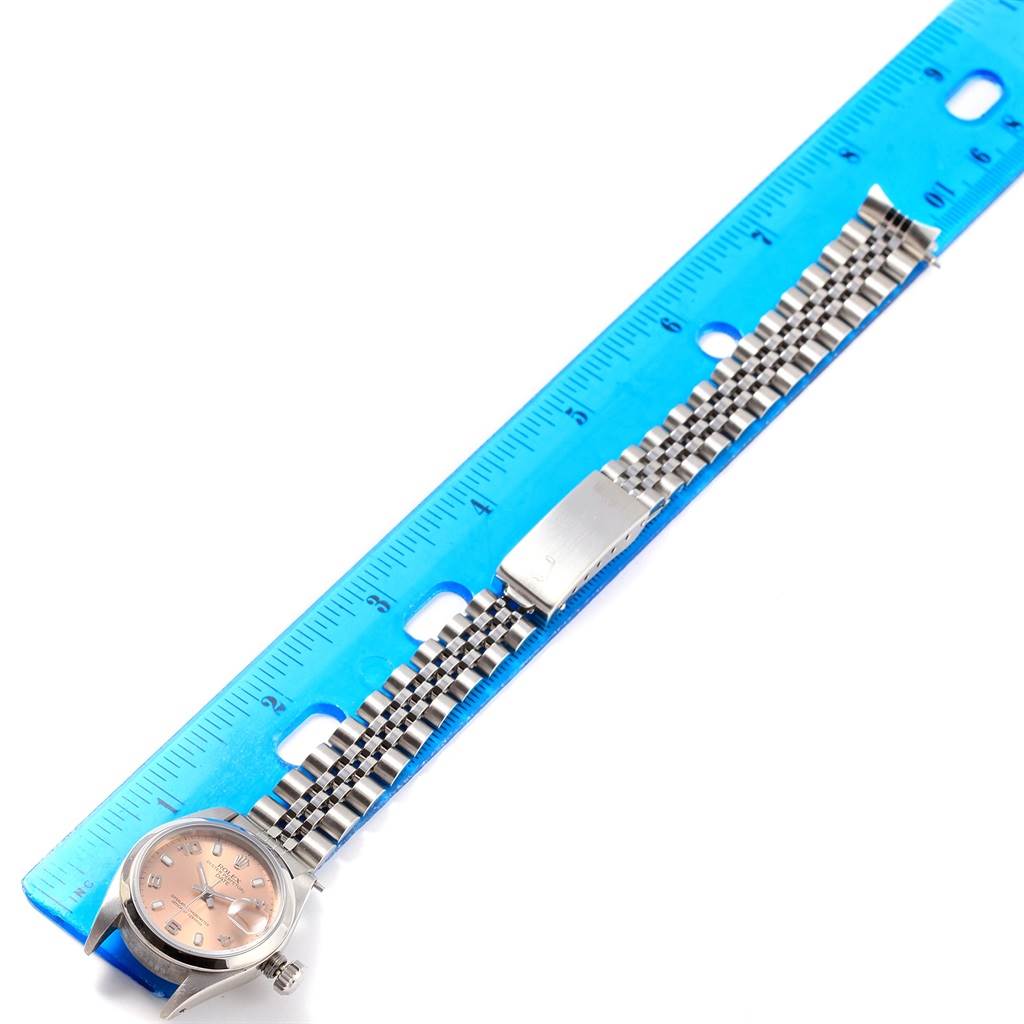 The Rolex Date 79160 Women's Stainless Steel Pink Dial 79160 Women's Stainless Steel Pink Dial model watch is shown from a top view, displaying the face, bracelet, and clasp, along a blue ruler for scale.