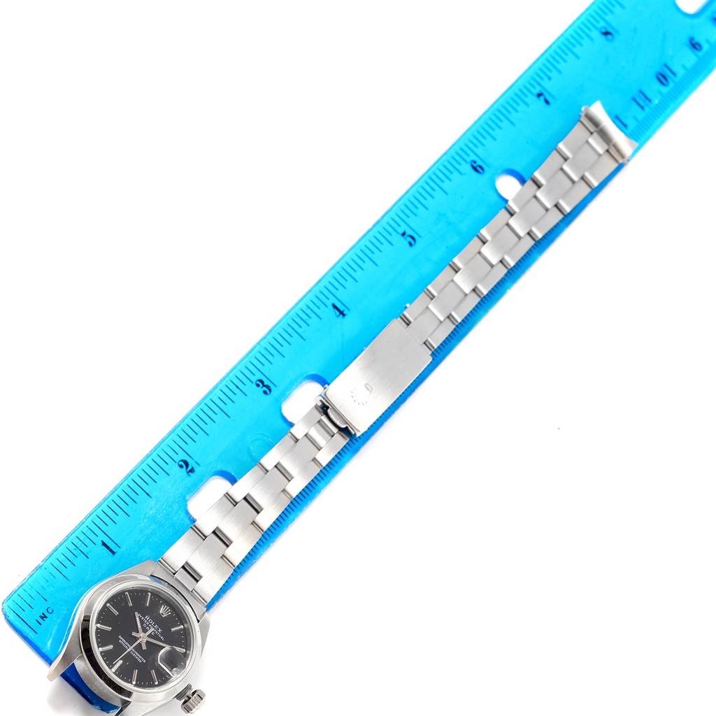 The image shows a Rolex Date 79160 Men's Stainless Steel Black Dial 79160 Men's Stainless Steel Black Dial model watch laid next to a blue ruler, highlighting its bracelet and clasp.