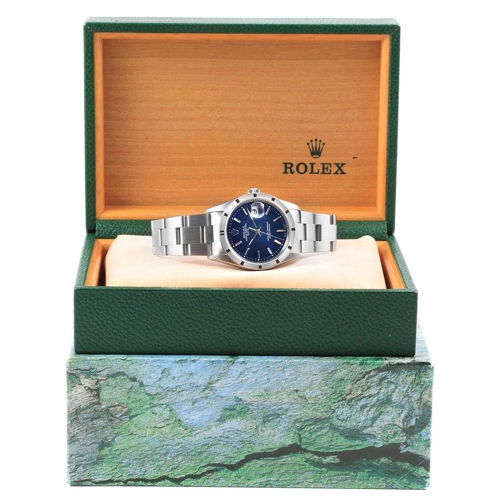 The image shows a Rolex Date 15210 Men's Stainless Steel Blue Dial 15210 Men's Stainless Steel Blue Dial model watch at a front angle, placed in an open Rolex box with a green exterior and orange interior.