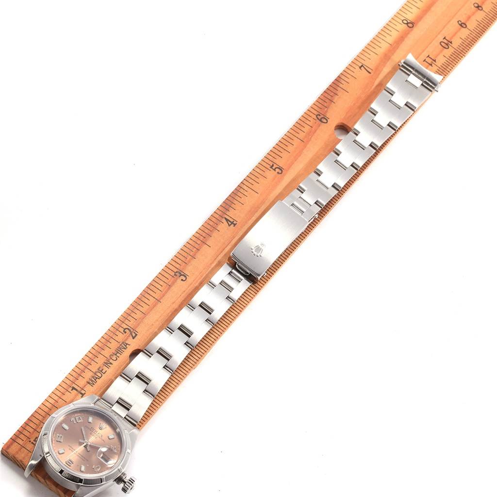 The Rolex Date 69190 Women's Stainless Steel Pink Dial 69190 Women's Stainless Steel Pink Dial model watch is shown at a top-down angle, with its face, bracelet, and clasp displayed next to a wooden ruler.