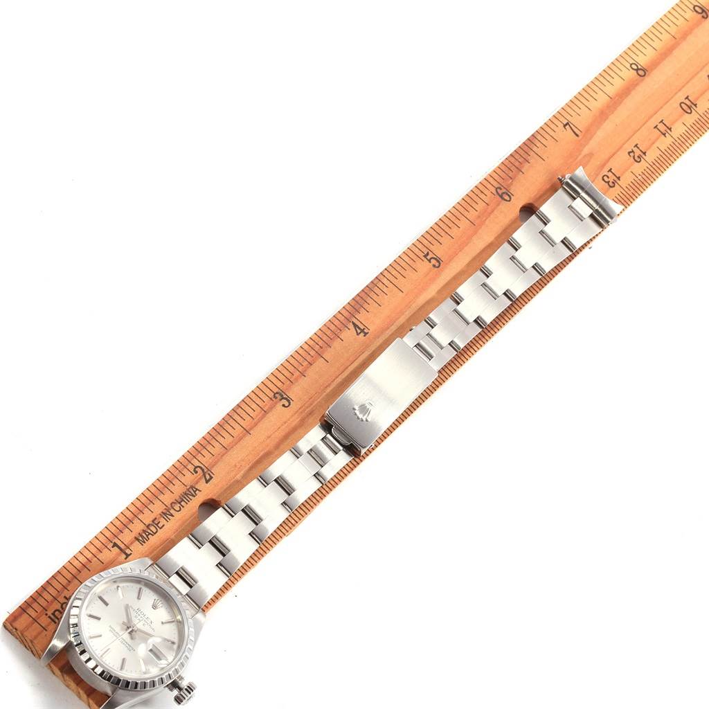 A Rolex Date 79240 Women's Stainless Steel Silver Dial 79240 Women's Stainless Steel Silver Dial watch with a silver band is laid flat beside a wooden ruler, showing the clasp, links, and watch face.