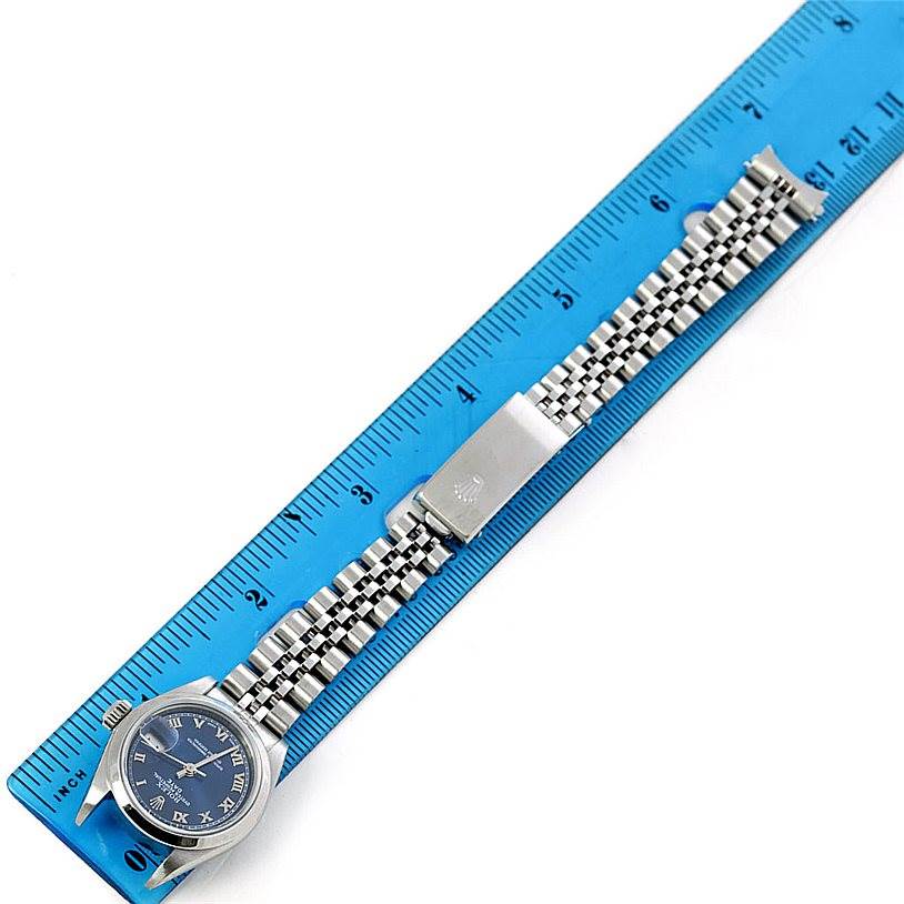 The Rolex Date 79160 Women's Stainless Steel Blue Dial 79160 Women's Stainless Steel Blue Dial model watch is shown flat, displaying the face, bracelet, and clasp alongside a blue ruler for scale.