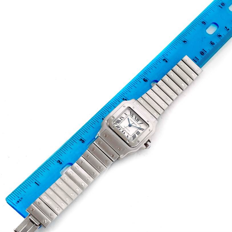 This image shows the entire Santos model by Cartier, including its face, crown, and metal bracelet, alongside a blue ruler for scale.