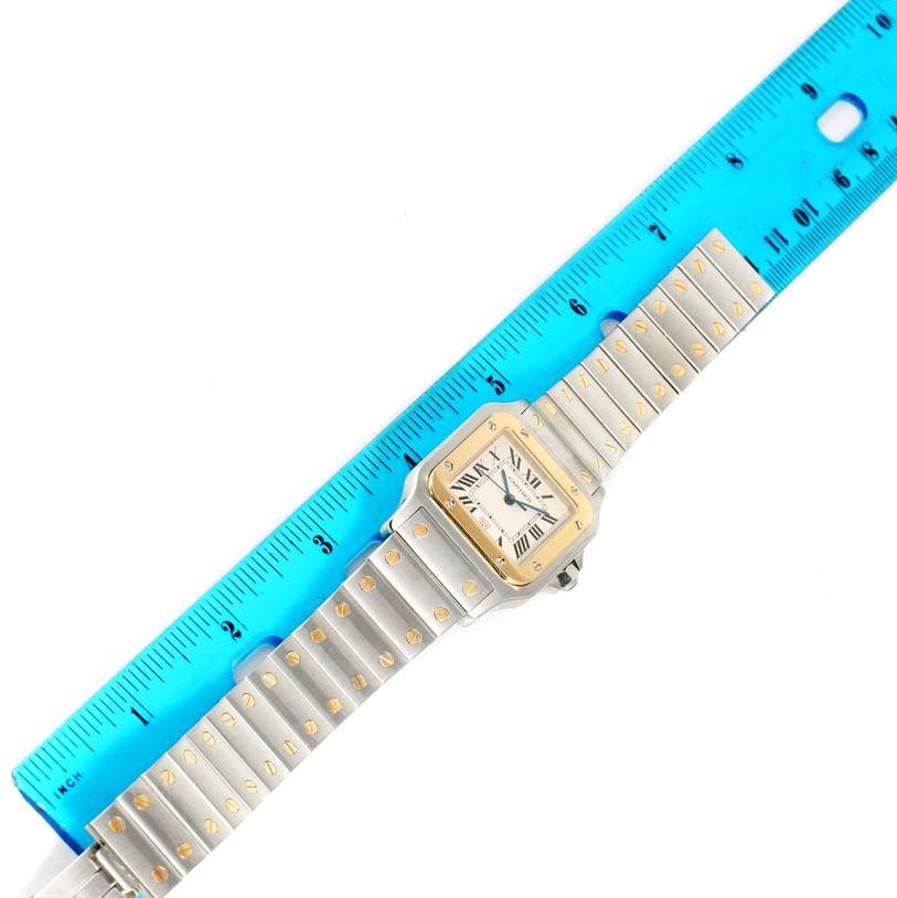 The Cartier Santos W20011C4 Men
s Stainless Steel Silver Dial W20011C4 Men
s Stainless Steel Silver Dial watch is shown from above, with the case, dial, bracelet, and part of a blue ruler for size reference.