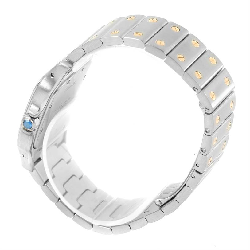 The image shows a side view of the Cartier Santos W20011C4 Stainless Steel Silver Dial W20011C4 Stainless Steel Silver Dial model watch, highlighting its bracelet with gold screws and a blue stone crown.