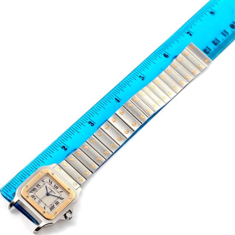 The Cartier Santos W20011C4 Stainless Steel Silver Dial W20011C4 Stainless Steel Silver Dial watch is shown lying flat with an extended metal bracelet next to a blue ruler for measurement.