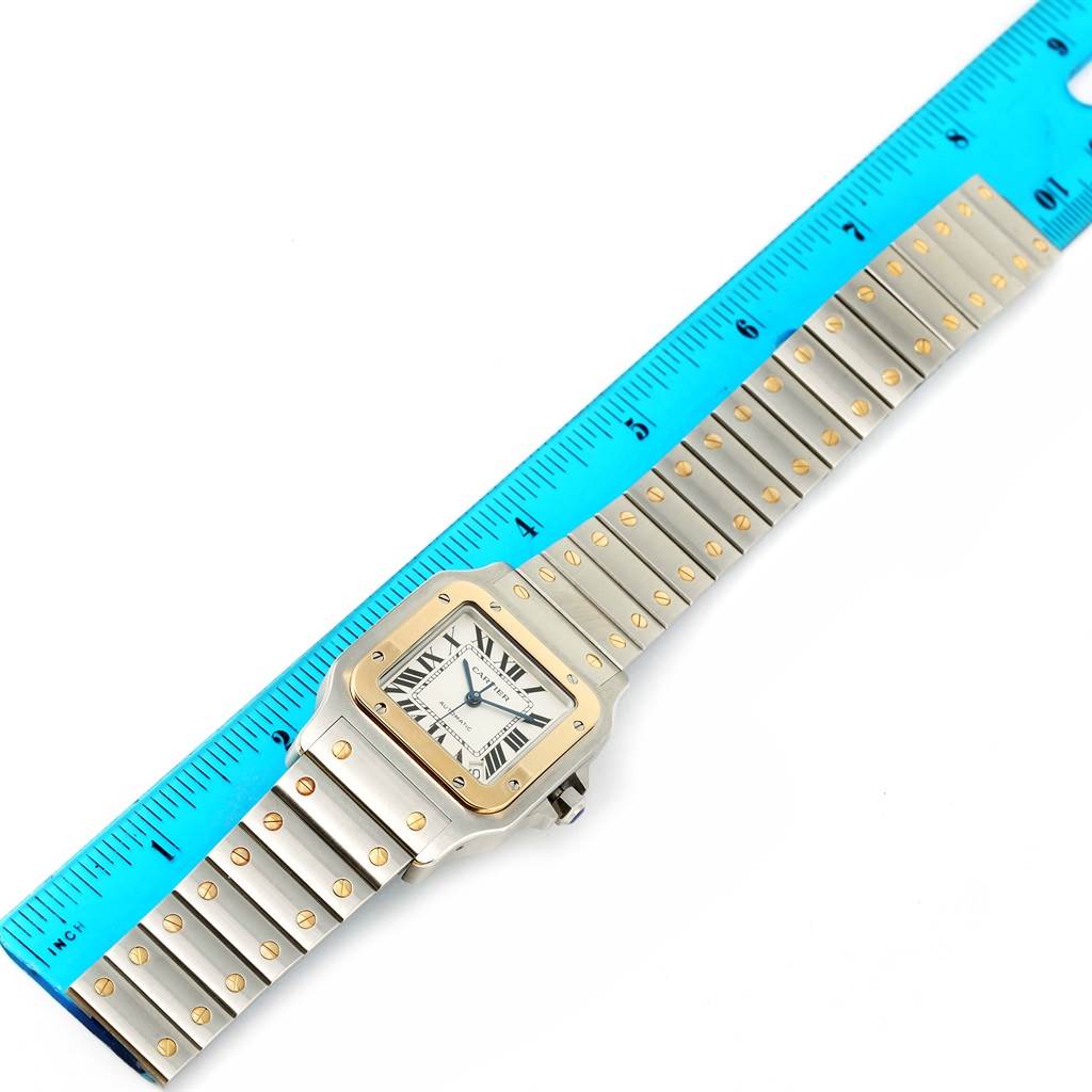 This image shows a Cartier Santos W20099C4 Men
s Stainless Steel Silver Dial W20099C4 Men
s Stainless Steel Silver Dial watch laid flat against a ruler, highlighting the face and metal bracelet.