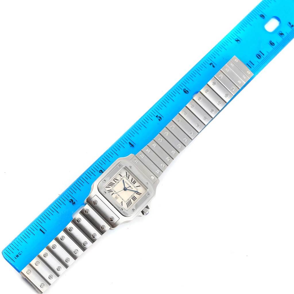 The image shows a top-down view of the Santos by Cartier watch, alongside a blue ruler for scale.