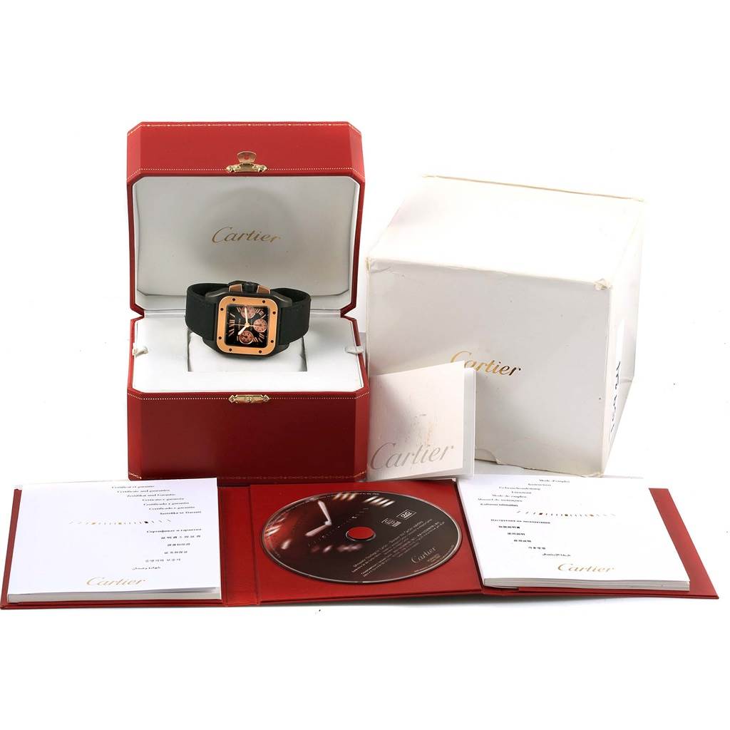 The image shows a Cartier Santos W2020004 Men's Titanium Black Dial W2020004 Men's Titanium Black Dial watch in its box along with packaging, a booklet, and a CD from a frontal angle.