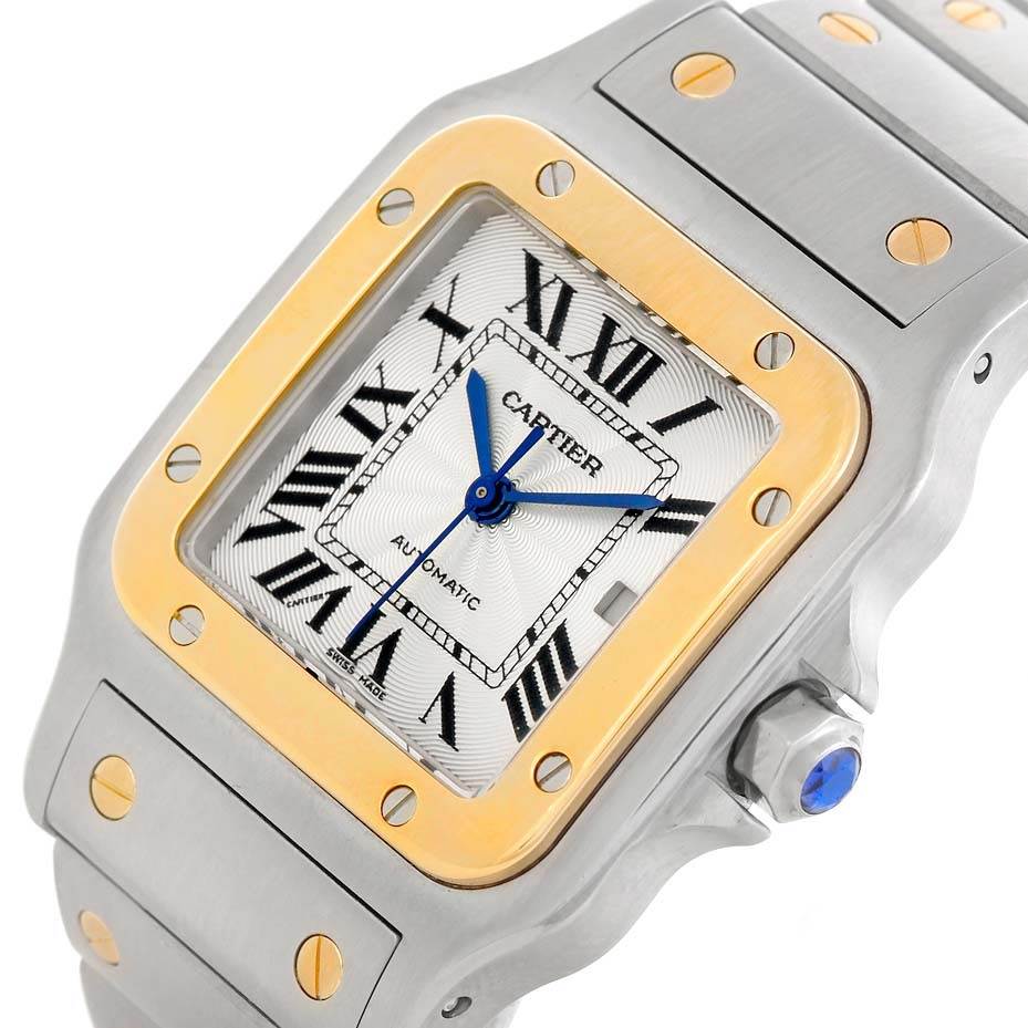 The image shows a Cartier Santos W20058C4 Stainless Steel Silver Dial W20058C4 Stainless Steel Silver Dial watch from an angled close-up, displaying its face, bezel, bracelet, and crown with a blue cabochon.