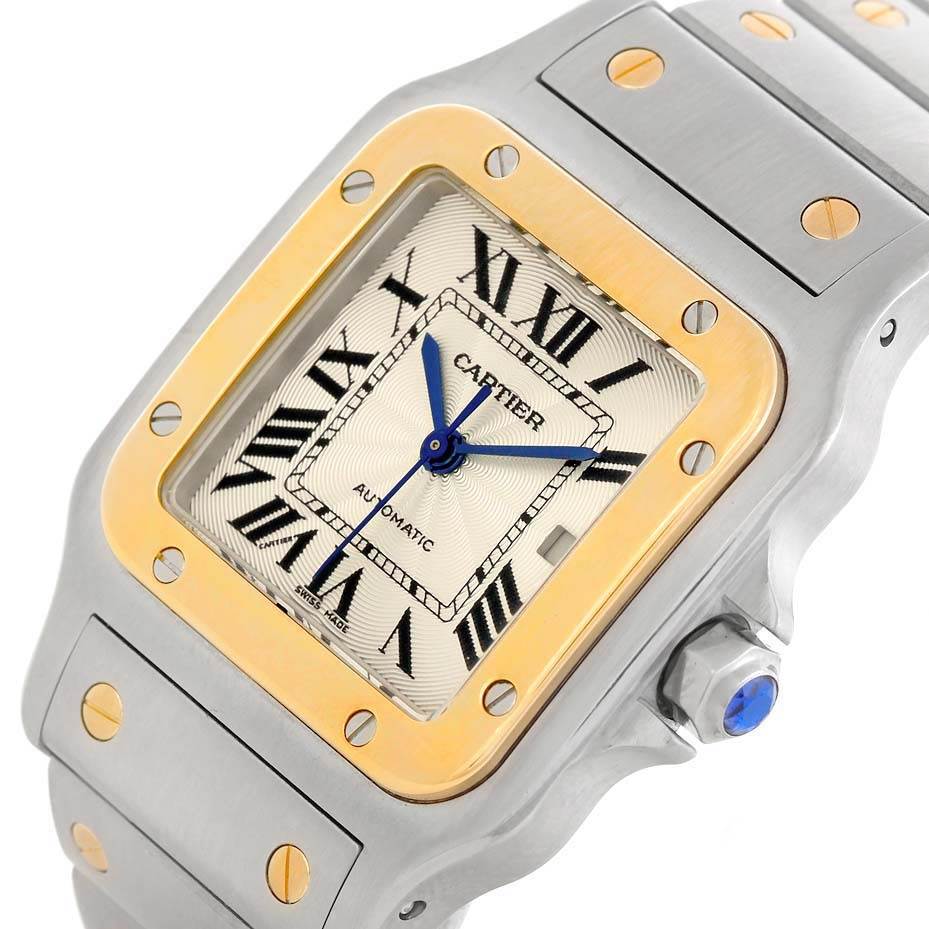 This image shows the face and strap of a Cartier Santos W20058C4 Men
s Stainless Steel Silver Dial W20058C4 Men
s Stainless Steel Silver Dial watch at an angle displaying its Roman numerals, gold bezel, and blue hands.
