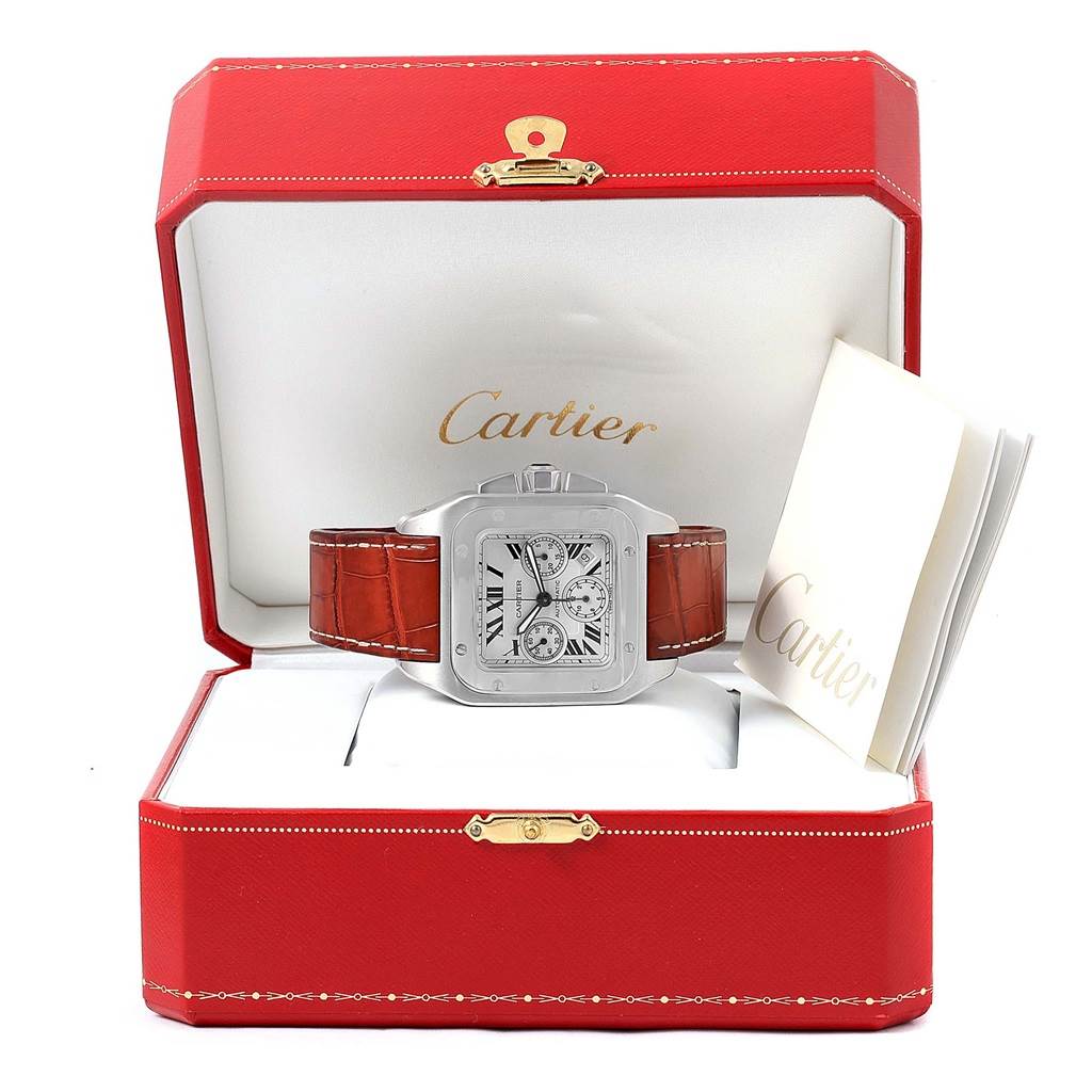 The Cartier Santos W20090X8 Men
s Stainless Steel Silver Dial W20090X8 Men
s Stainless Steel Silver Dial watch is shown from a front angle, inside an open red box with papers beside it.