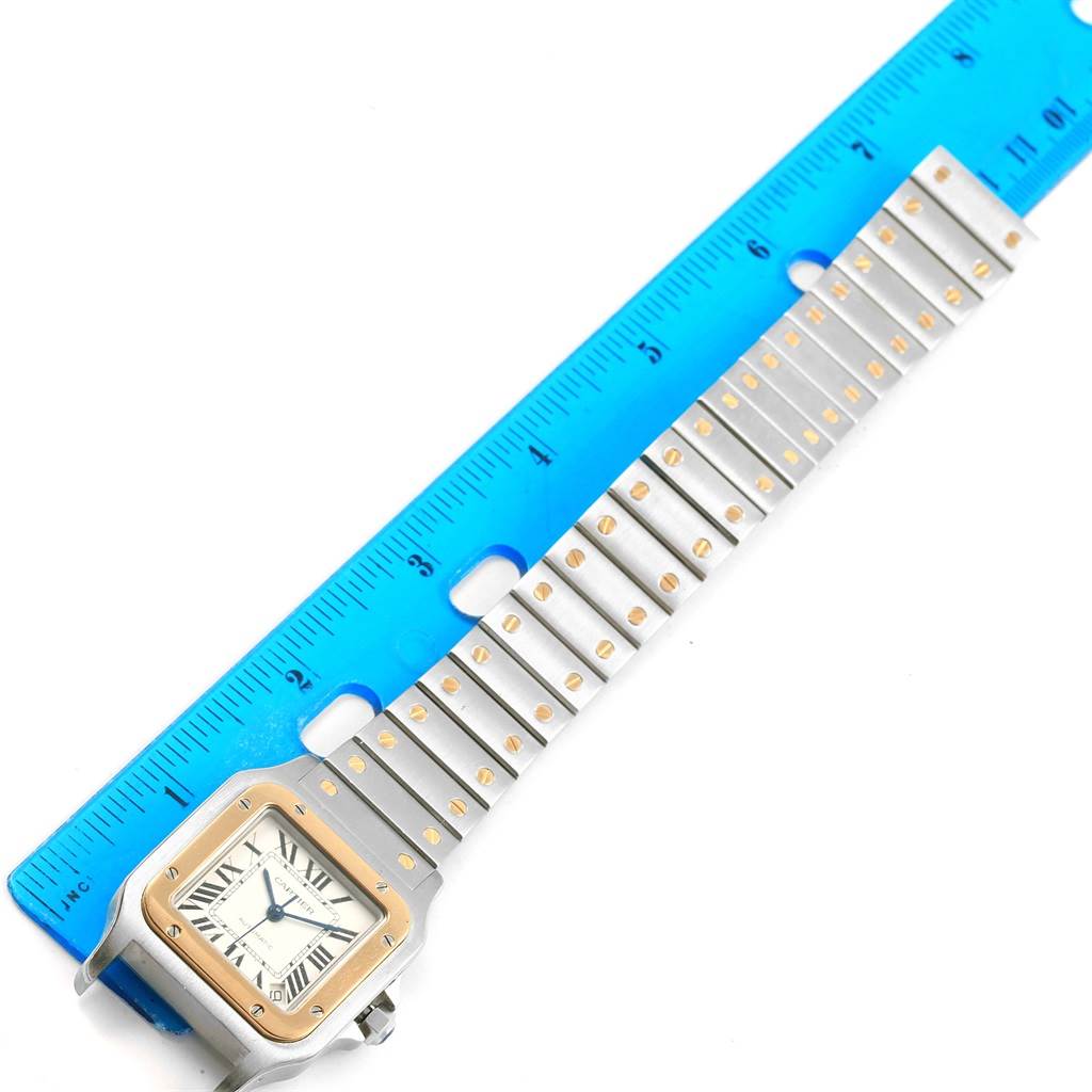 The Cartier Santos W20099C4 Men's Stainless Steel Silver Dial W20099C4 Men's Stainless Steel Silver Dial watch is shown at a top-down angle, displaying the face and band next to a blue ruler.