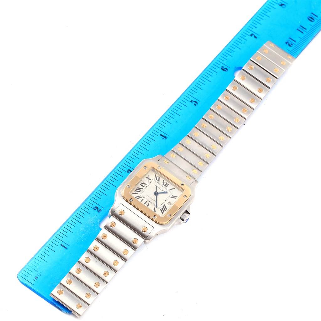 The Cartier Santos W20058C4 Stainless Steel Silver Dial W20058C4 Stainless Steel Silver Dial watch is shown from an overhead angle, displaying the face and the full length of the band next to a blue ruler.