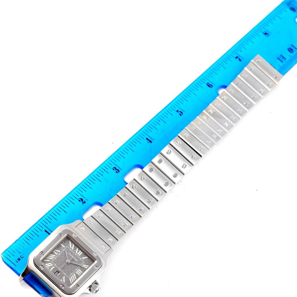 The image shows a Santos model by Cartier watch laid flat alongside a blue ruler.