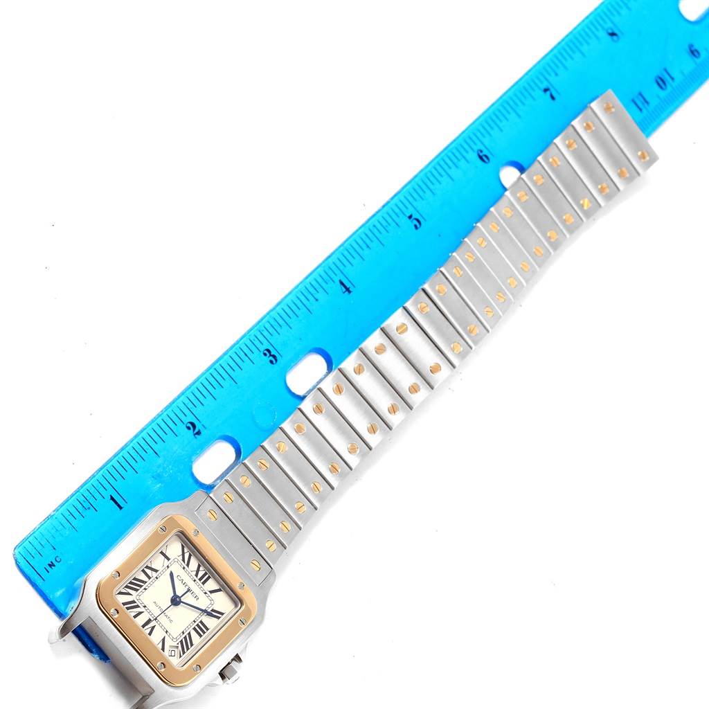This image shows the Santos model by Cartier lying flat next to a ruler, highlighting the face and the metal bracelet.