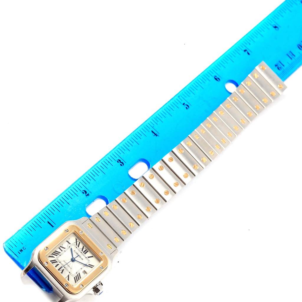 The image shows a top-down view of the Cartier Santos W20058C4 Men's Stainless Steel Silver Dial W20058C4 Men's Stainless Steel Silver Dial watch, featuring its square face and metal bracelet next to a ruler.