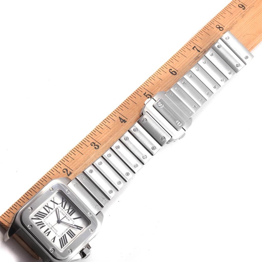 The image shows a Santos de Cartier watch laid flat with a ruler next to it, displaying its face and bracelet.