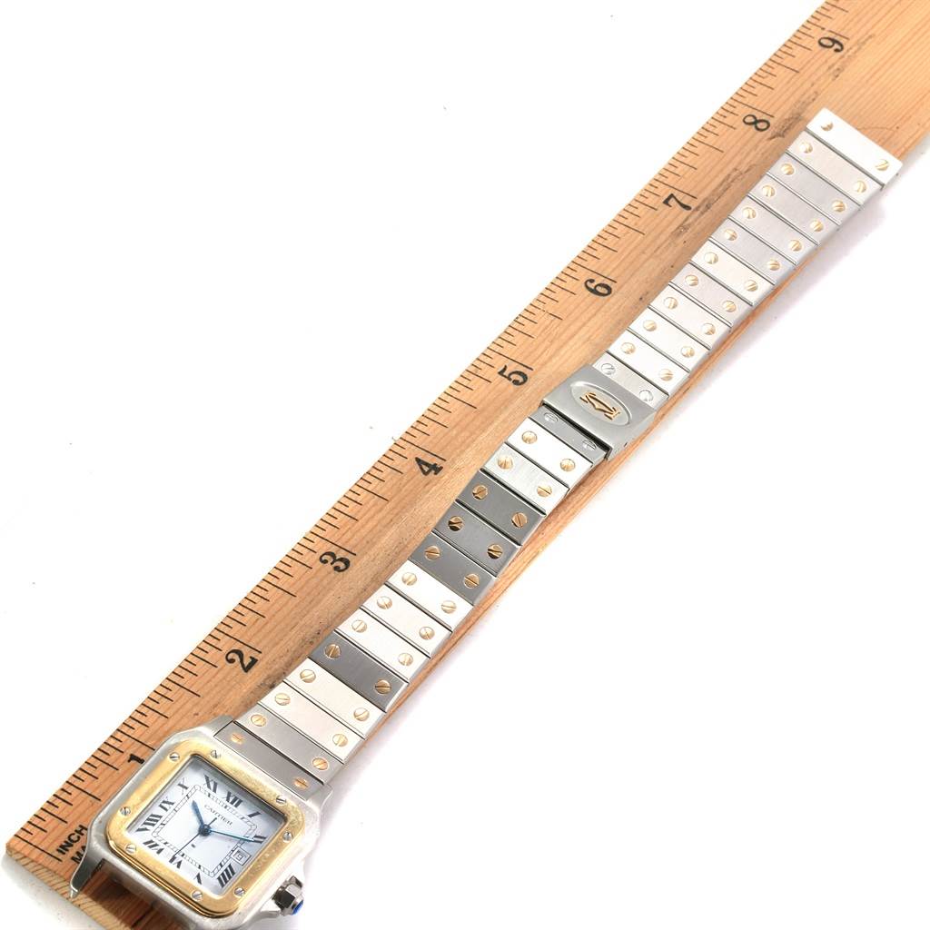 This image shows the Cartier Santos 1172961 Men
s Stainless Steel White Dial 1172961 Men
s Stainless Steel White Dial watch lying flat next to a ruler, displaying the face, bracelet, and clasp.