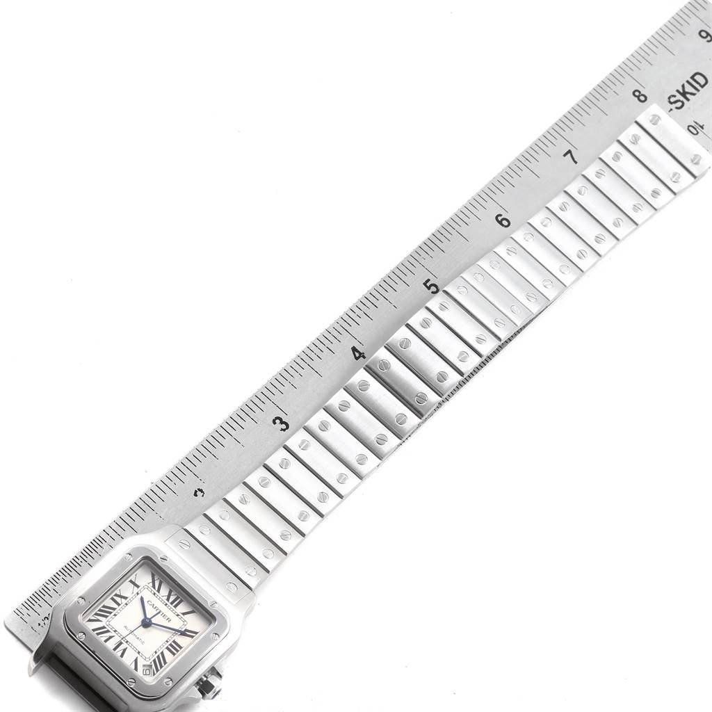 The image shows a Cartier Santos W20098D6 Men
s Stainless Steel Silver Dial W20098D6 Men
s Stainless Steel Silver Dial watch with its face and a portion of the metal bracelet next to a ruler for measurement.