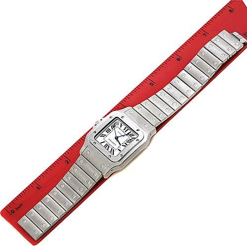 The Cartier Santos W20098D6 Stainless Steel Silver Dial W20098D6 Stainless Steel Silver Dial watch is shown from a top-down angle, displaying its full face and metal bracelet on a red ruler for scale.