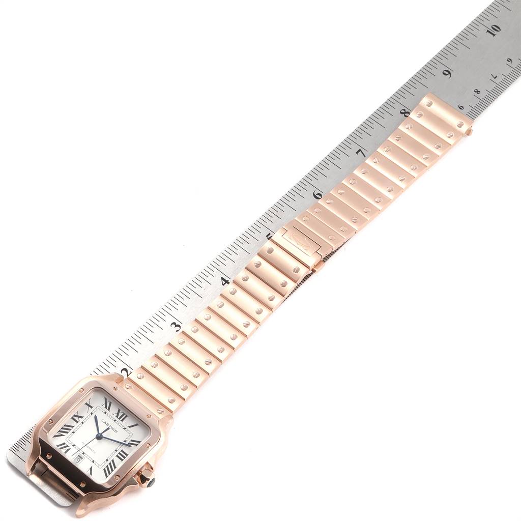 The image shows a Santos model Cartier watch laid flat next to a ruler, highlighting its face and band.