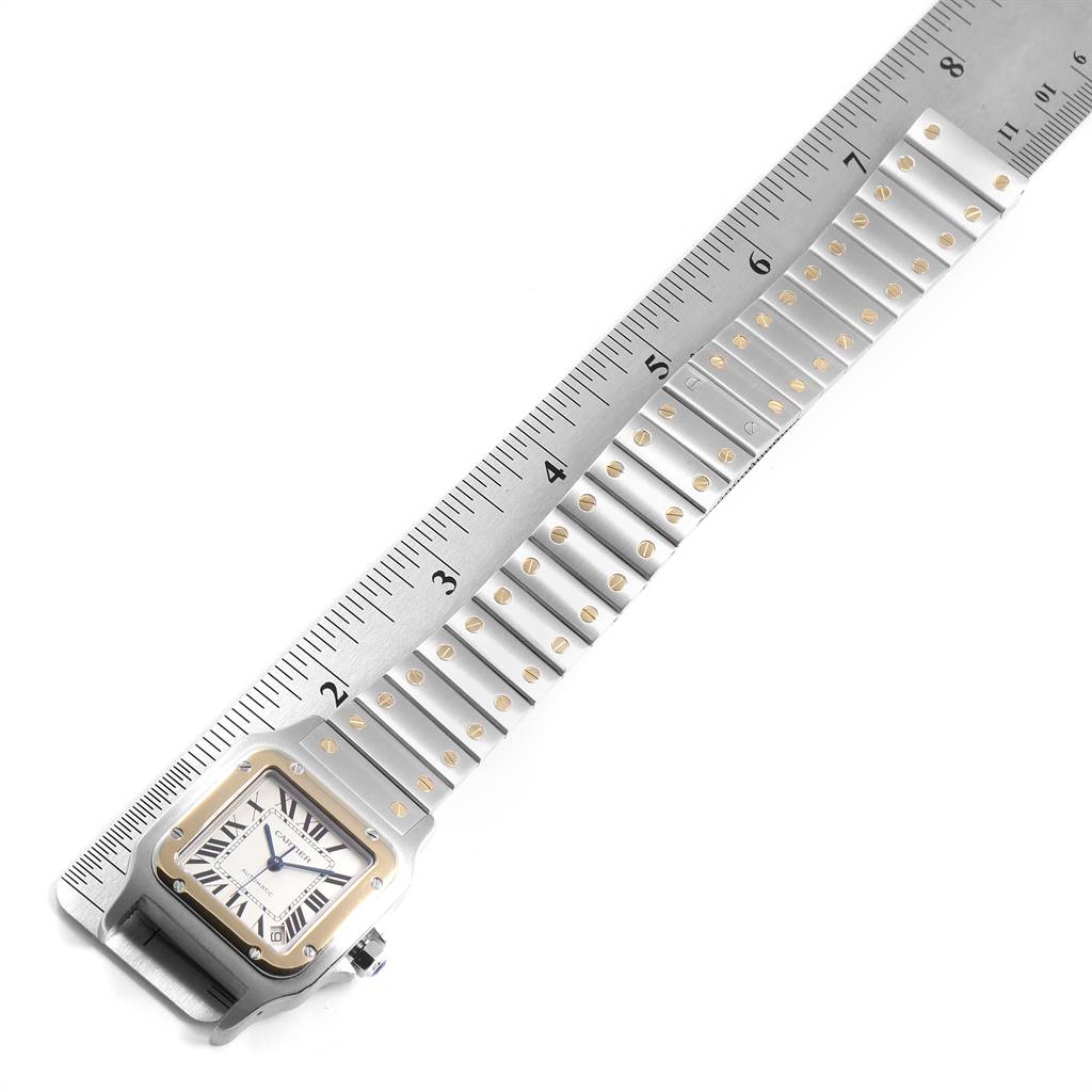The image shows a Santos model Cartier watch placed next to a ruler, highlighting its bracelet and case from a top-down angle.