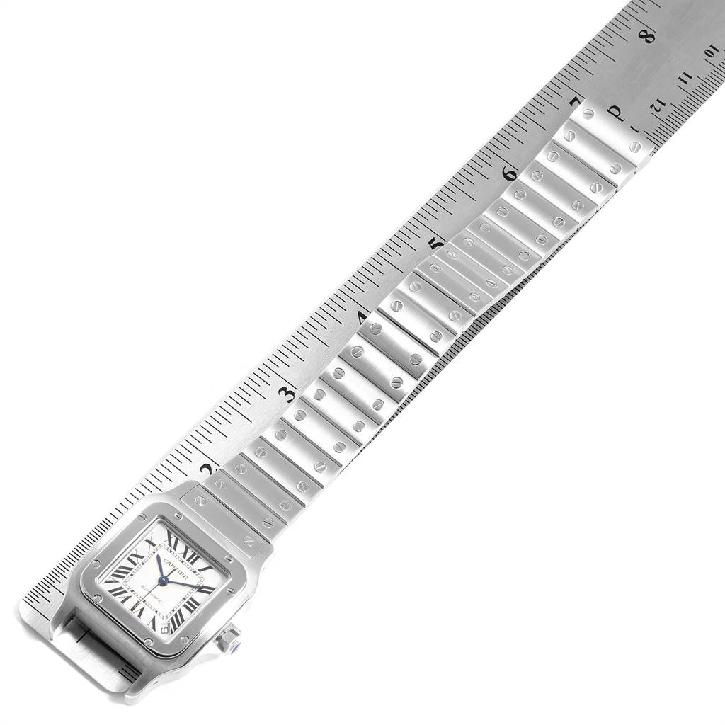 The image shows the Santos de Cartier watch placed diagonally next to a ruler, displaying part of its face and the bracelet.