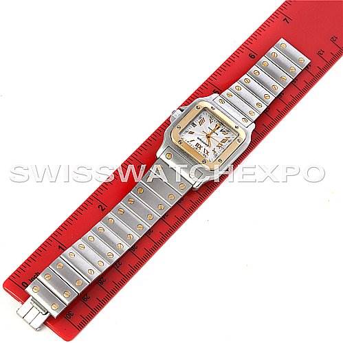 The image shows a top-down view of the Santos model watch by Cartier, fully extended next to a red ruler for scale.