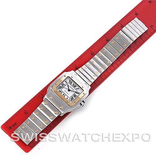 The image shows a top view of a Santos model by Cartier, including its square face and linked strap, placed against a red ruler.