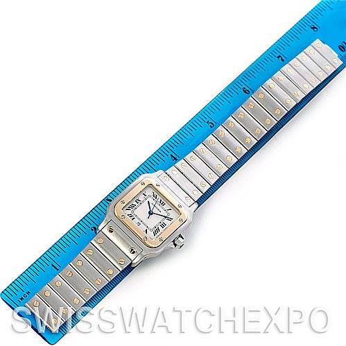 The Cartier Santos W20011C4 Men
s Stainless Steel Silver Dial W20011C4 Men
s Stainless Steel Silver Dial watch is shown horizontally, with its face and metal bracelet with gold accents visible alongside a blue ruler for scale.