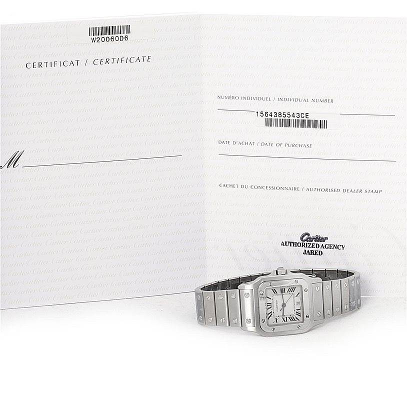 The image shows a Cartier Santos W20060D6 Men
s Stainless Steel Silver Dial W20060D6 Men
s Stainless Steel Silver Dial watch lying flat, with its certificate booklet displayed behind it.