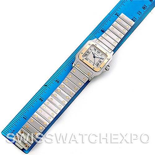 The image shows a top-down view of a Cartier Santos W20011C4 Men's Stainless Steel Silver Dial W20011C4 Men's Stainless Steel Silver Dial watch, highlighting the entire face, bezel, and bracelet with gold screws, alongside a blue ruler for scale.