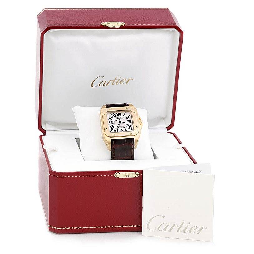 The Cartier Santos W20071Y1 Men's Yellow Gold Silver Dial W20071Y1 Men's Yellow Gold Silver Dial watch is shown in an open red box, with its dial and leather strap visible, accompanied by a booklet.