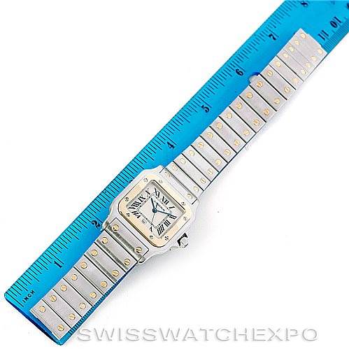 The image shows a top view of a Cartier Santos W20011C4 Men
s Stainless Steel Silver Dial W20011C4 Men
s Stainless Steel Silver Dial watch, including its face and full bracelet, placed alongside a blue ruler.