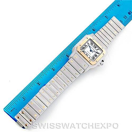 The image shows a top-down view of a Cartier Santos W20099C4 Men
s Stainless Steel Silver Dial W20099C4 Men
s Stainless Steel Silver Dial watch next to a blue ruler, displaying the entire watch including the face, case, and bracelet.