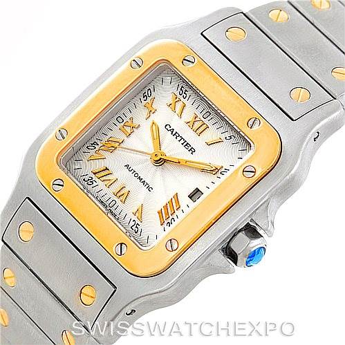 The image shows a close-up angle of a Santos model Cartier watch, focusing on its face, bezel, and bracelet with a blue cabochon crown.