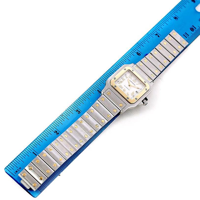 The image shows a full Santos model watch by Cartier, laid flat alongside a blue ruler.