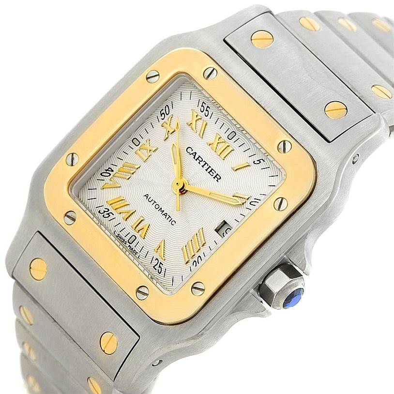The Cartier Santos W20058C4 Men
s Stainless Steel Silver Dial W20058C4 Men
s Stainless Steel Silver Dial watch is shown at an angled close-up, highlighting its gold bezel, square face, Roman numerals, and metal bracelet.
