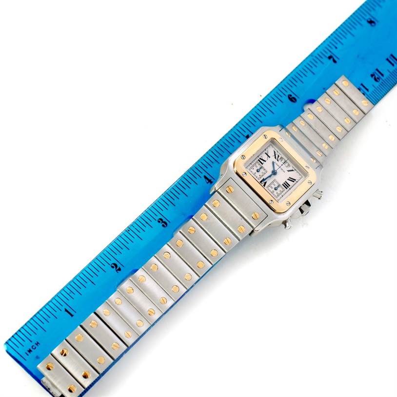 The image shows a Cartier Santos W20042C4 Men
s Stainless Steel Silver Dial W20042C4 Men
s Stainless Steel Silver Dial watch laid flat next to a blue ruler, showcasing the face and full length of the bracelet.