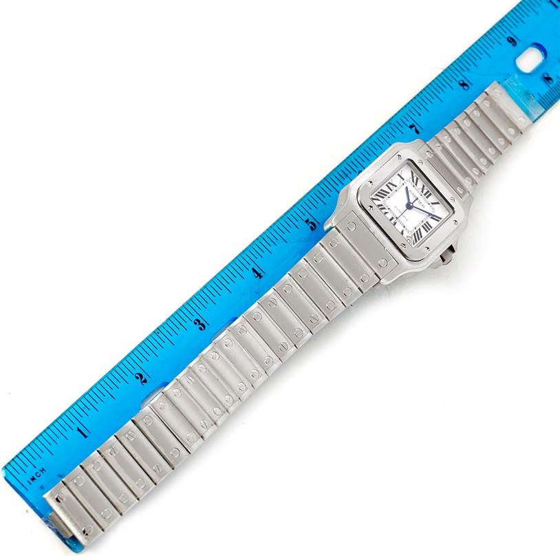 The Cartier Santos W20098D6 Men
s Stainless Steel Silver Dial W20098D6 Men
s Stainless Steel Silver Dial watch is shown flat and measured against a blue ruler, displaying its face and metal bracelet.